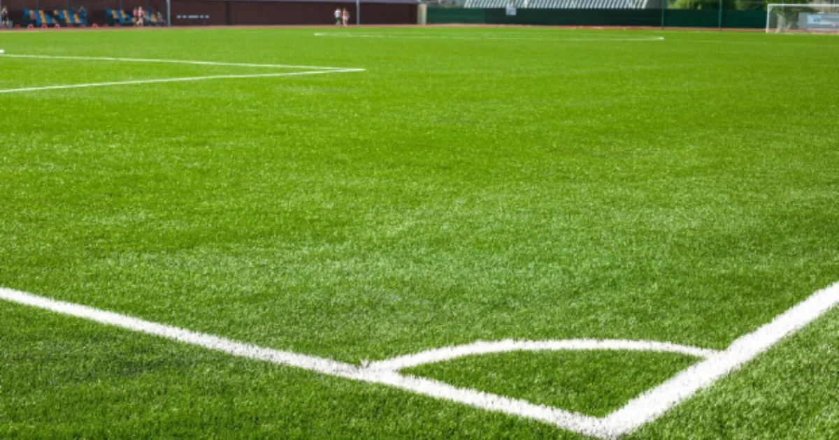 A freshly painted corner of a synthetic grass soccer field under clear skies.